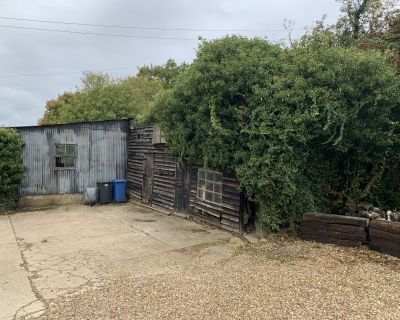View of the old, dilapidated outbuildings before renovation, with overgrown vegetation and weathered timber.
