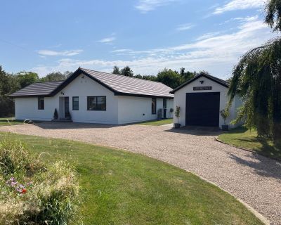 Completed refurbishment of a 1980s bungalow with modern features and updated facade, surrounded by a landscaped garden.
