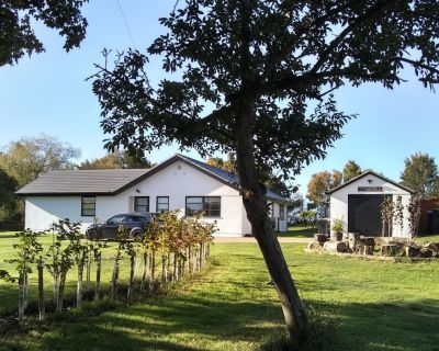 Refurbished 1980s bungalow with updated facade and modern garage, surrounded by a gravel driveway.